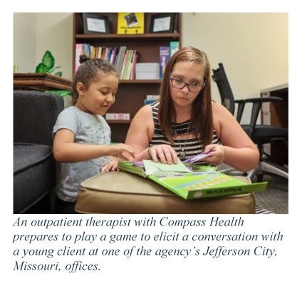Photo of a Compass Health outpatient therapist with a child. Caption states an outpatient therapist with Compass Health prepares to play a game to elicit a conversation with a young client at one of the agency's Jefferson City, Missouri, offices.