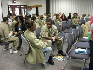 Photograph of a couple's workshop held for incarcerated men and their partners in an Indiana state prison.  The photograph shows individual couples sitting side by side and communicating with one another, with a facilitator at the back of the room.
