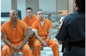 Picture of three inmates listening to a corrections officer.